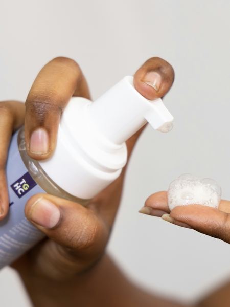 Mains appliquant une mousse nettoyante anti-acné