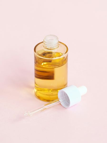 Sérum anti-taches ambré et sa pipette sur fond rose