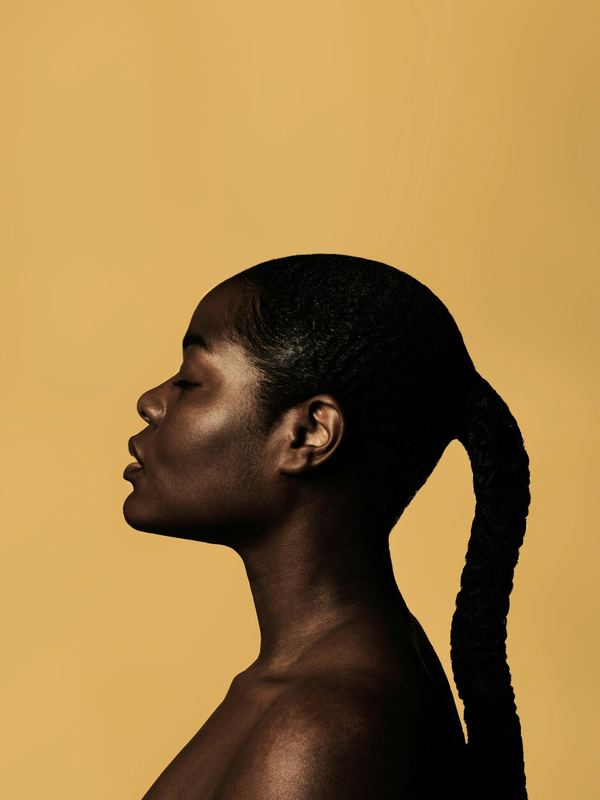 Femme à la peau foncée de profil, peau saine et lumineuse, sur fond doré